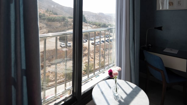 A room with a large window, a small round table with a vase, and a desk with a chair. - Petra Boutique Hotel (Wadi Musa)