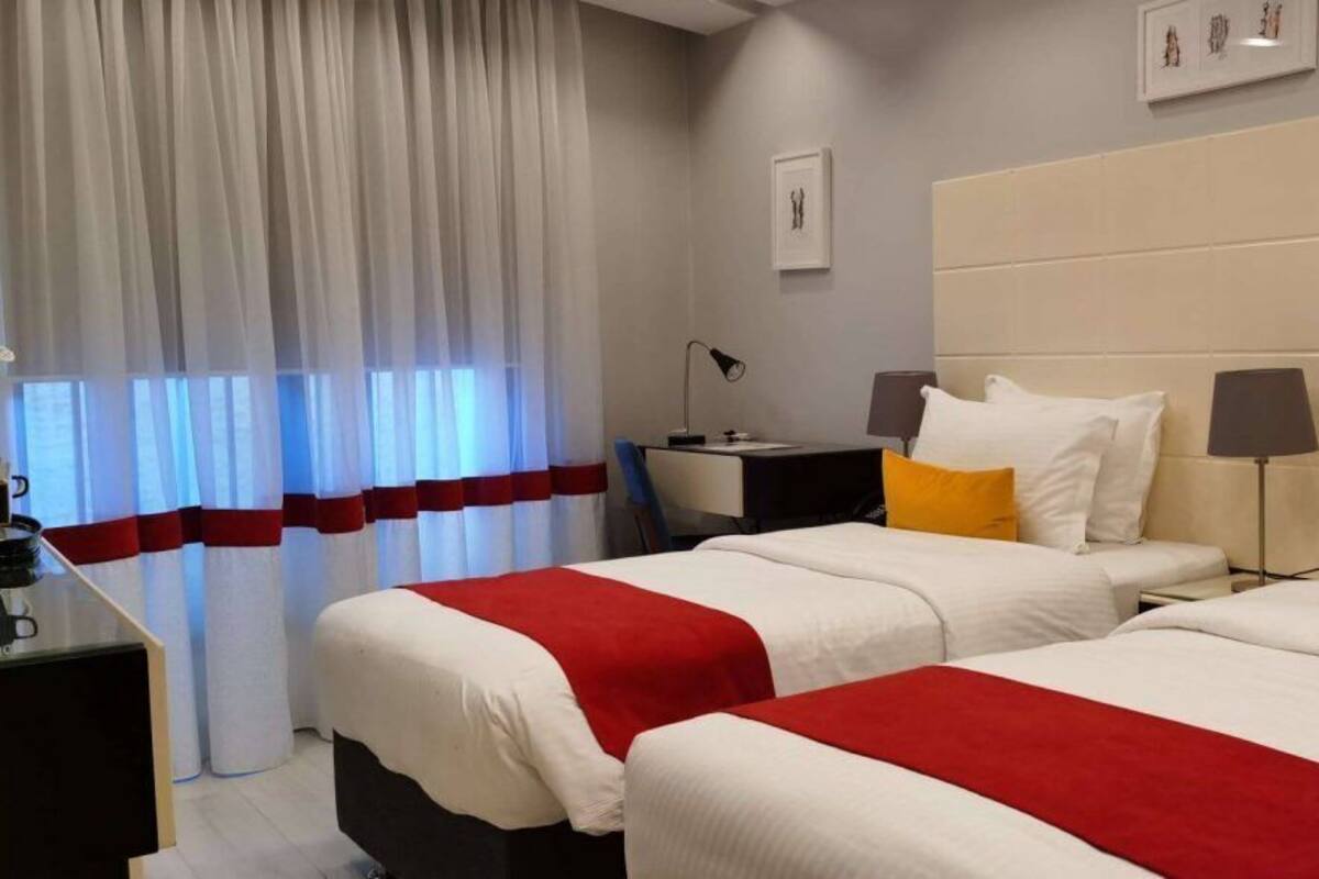 A hotel room with two beds, a desk, a chair, a lamp, and a curtain.