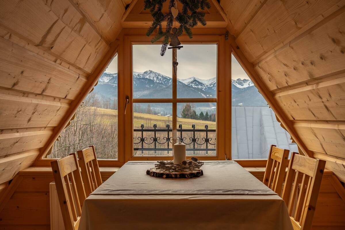 A wooden interior with a table and chairs, a large window with a view of mountains, and a decorative item on the table.