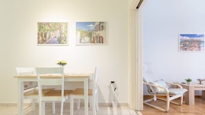 A dining area with a wooden table and chairs, a vase with flowers, and two framed pictures on the wall. - Cozy Flat in hip Koukaki (Athens)