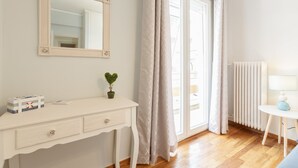 A room with a white dresser, a mirror, a small plant, a radiator, and a window with curtains. - Cozy Flat in hip Koukaki (Athens)