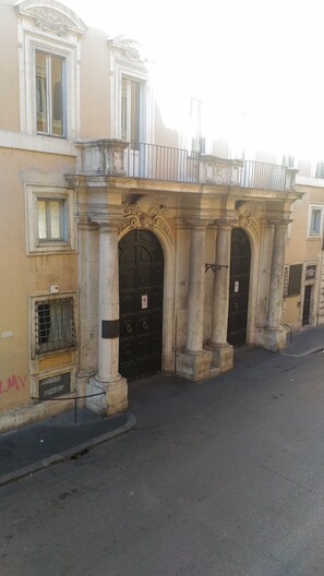 Un edificio con tres puertas negras, cada una con un letrero encima. Hay ventanas en los pisos superiores y una barandilla de metal en el balcón.