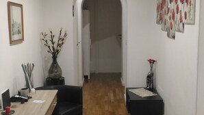 A modern dining area with a wooden floor, a dining table, and black chairs. There is a vase with branches and a framed picture on the wall. An archway leads to another room. - Domus Del Corso Spagna (Rome)