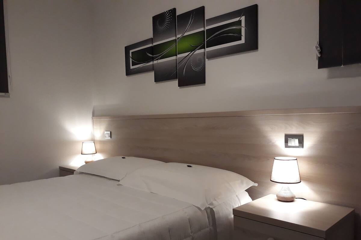 A hotel room with a bed, two bedside tables with lamps, and a wall-mounted artwork.