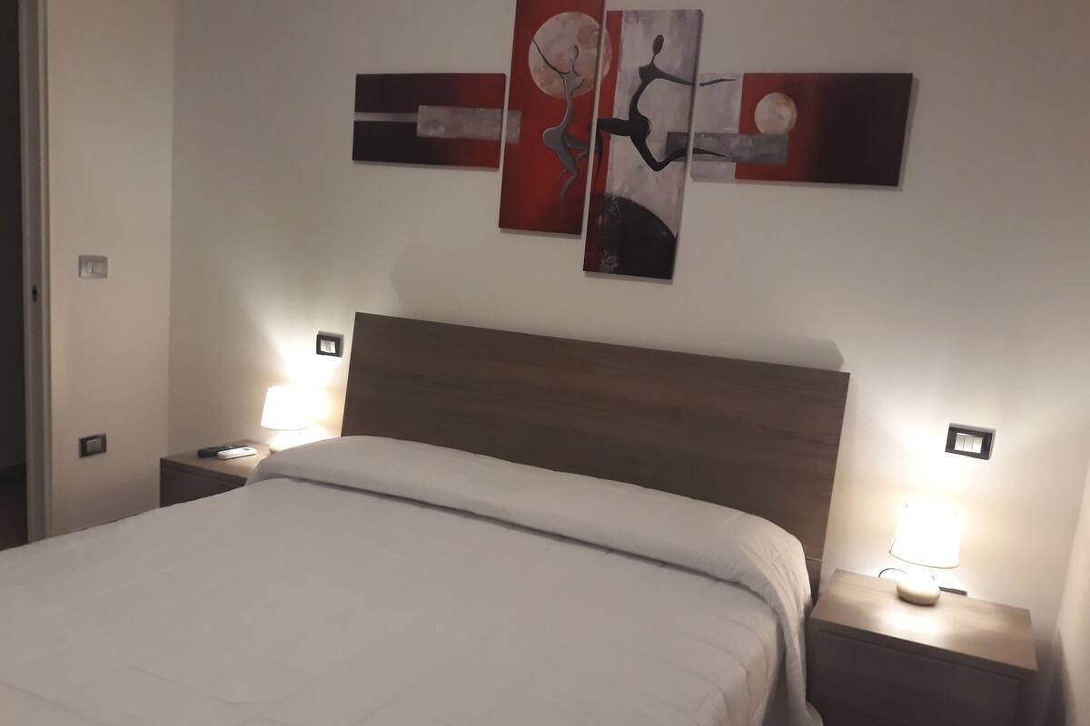 A hotel room with a large bed, two bedside tables with lamps, and abstract wall art.