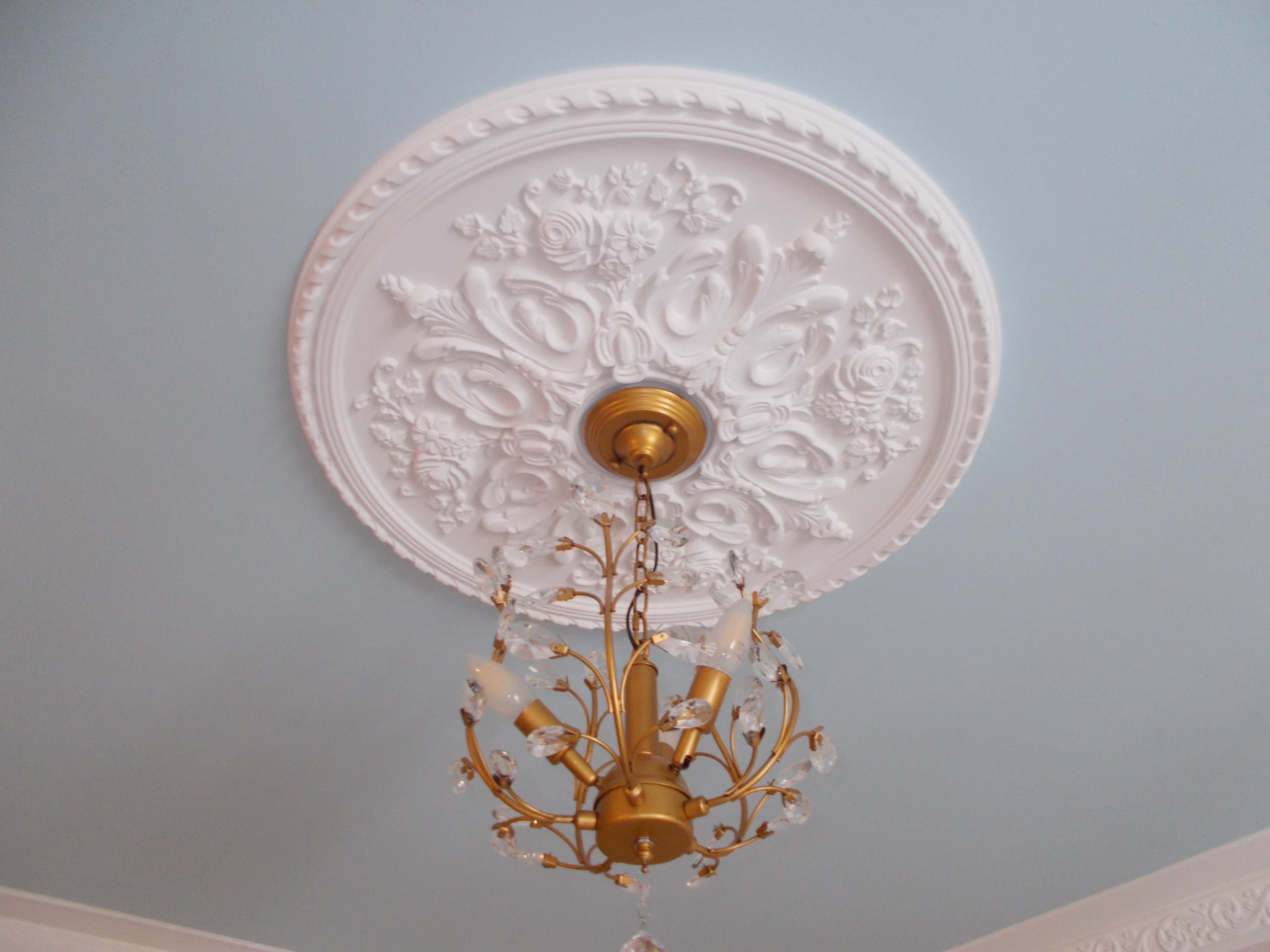 A ceiling with an ornate white panel and a chandelier with gold accents.