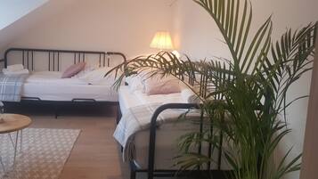 A cozy bedroom with two beds, a bedside lamp, a small table, and a large potted plant.