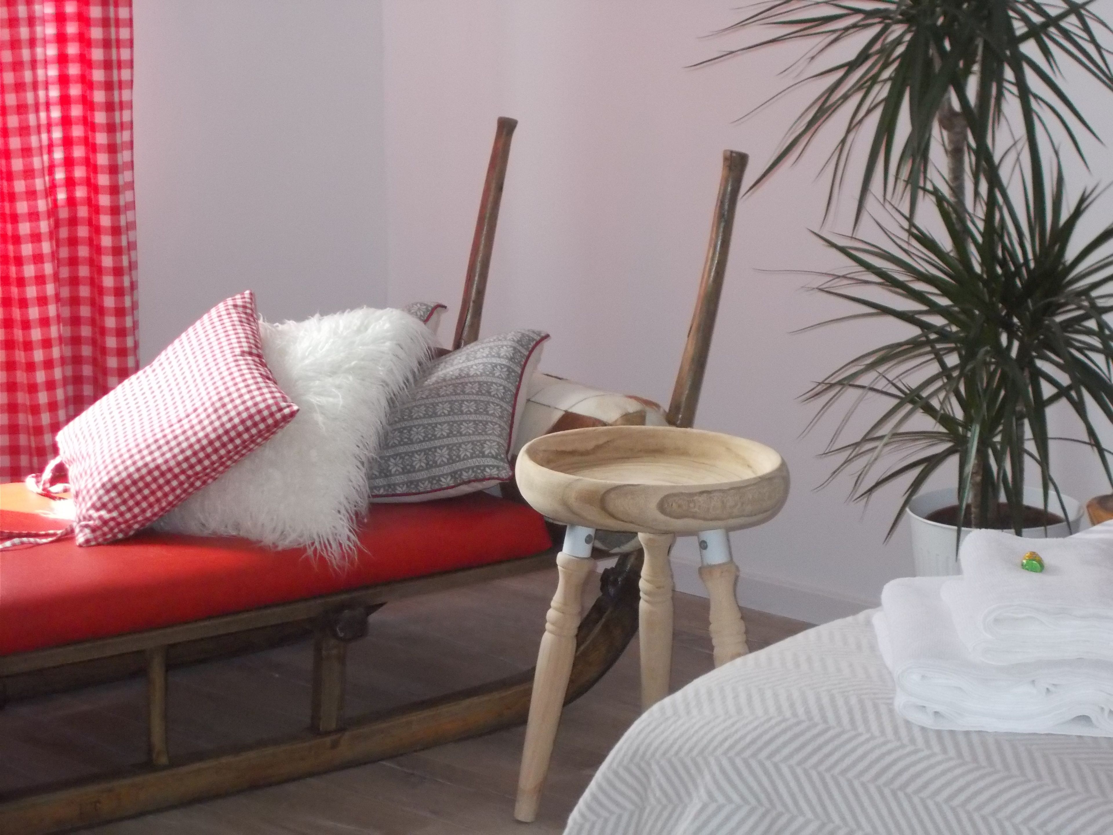 Una habitación con un sofá rojo, un almohadón mullido blanco, un almohadón estampado, un cuenco de madera, una planta en maceta y una cama con ropa de cama blanca.