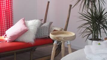 Una habitación con un sofá rojo, un almohadón mullido blanco, un almohadón estampado, un cuenco de madera, una planta en maceta y una cama con ropa de cama blanca.