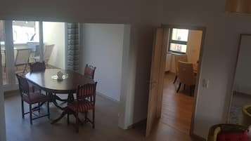 A dining area with a table and chairs, a view through an open door to a kitchen, and a window with curtains.