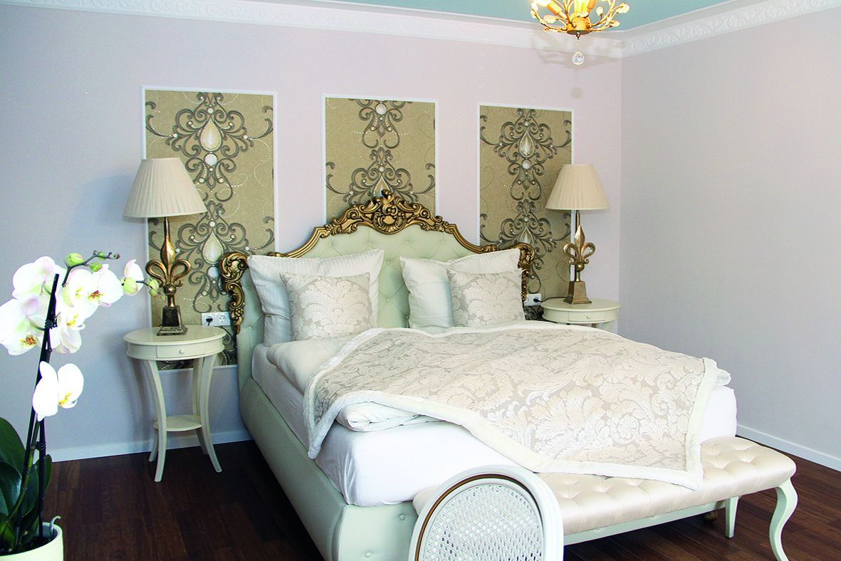 Un dormitorio con cama, dos mesitas de noche, lámparas y un panel decorativo en la pared.