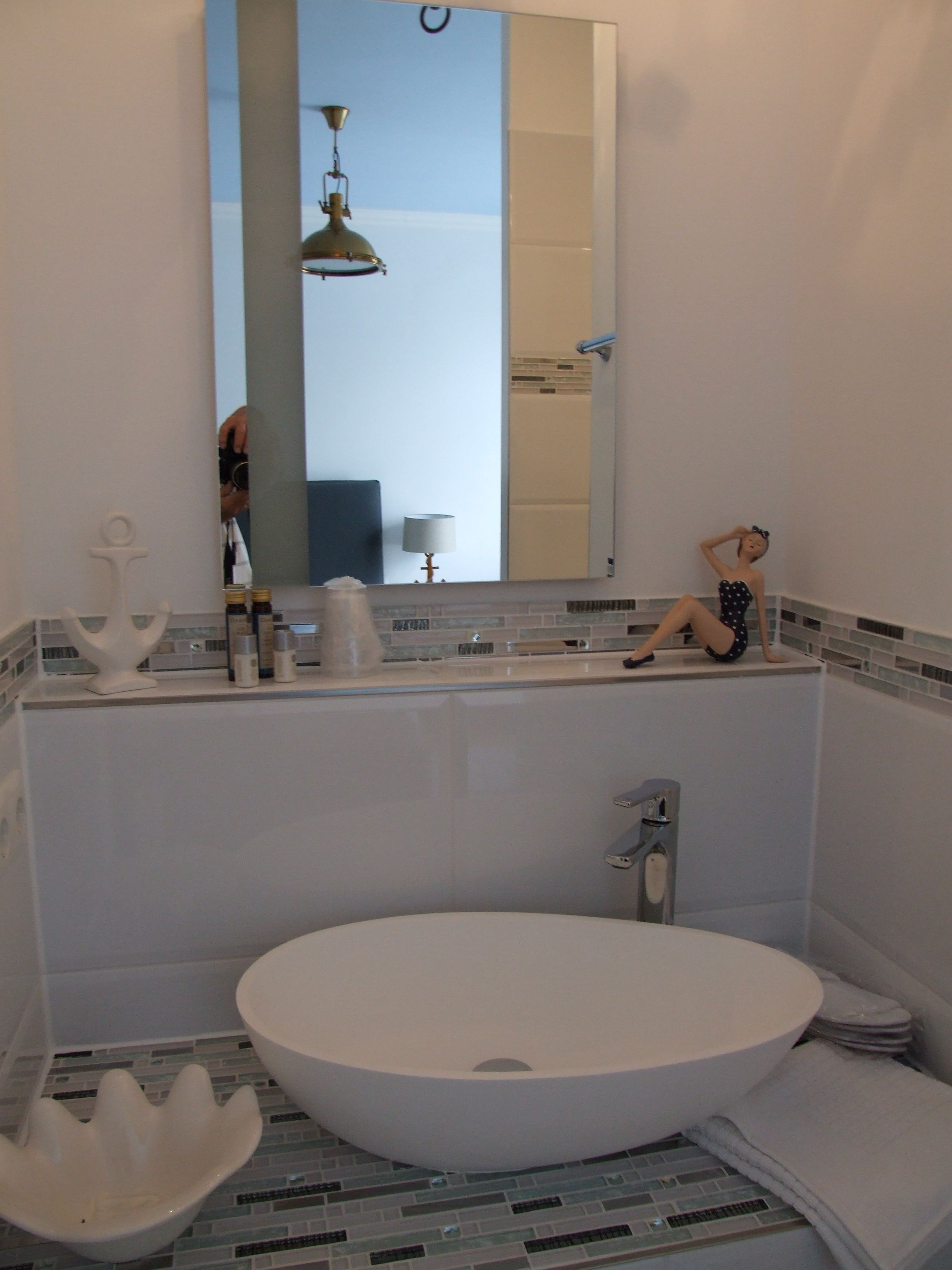 A modern bathroom with a large oval sink, a mirror, and a hanging light fixture.