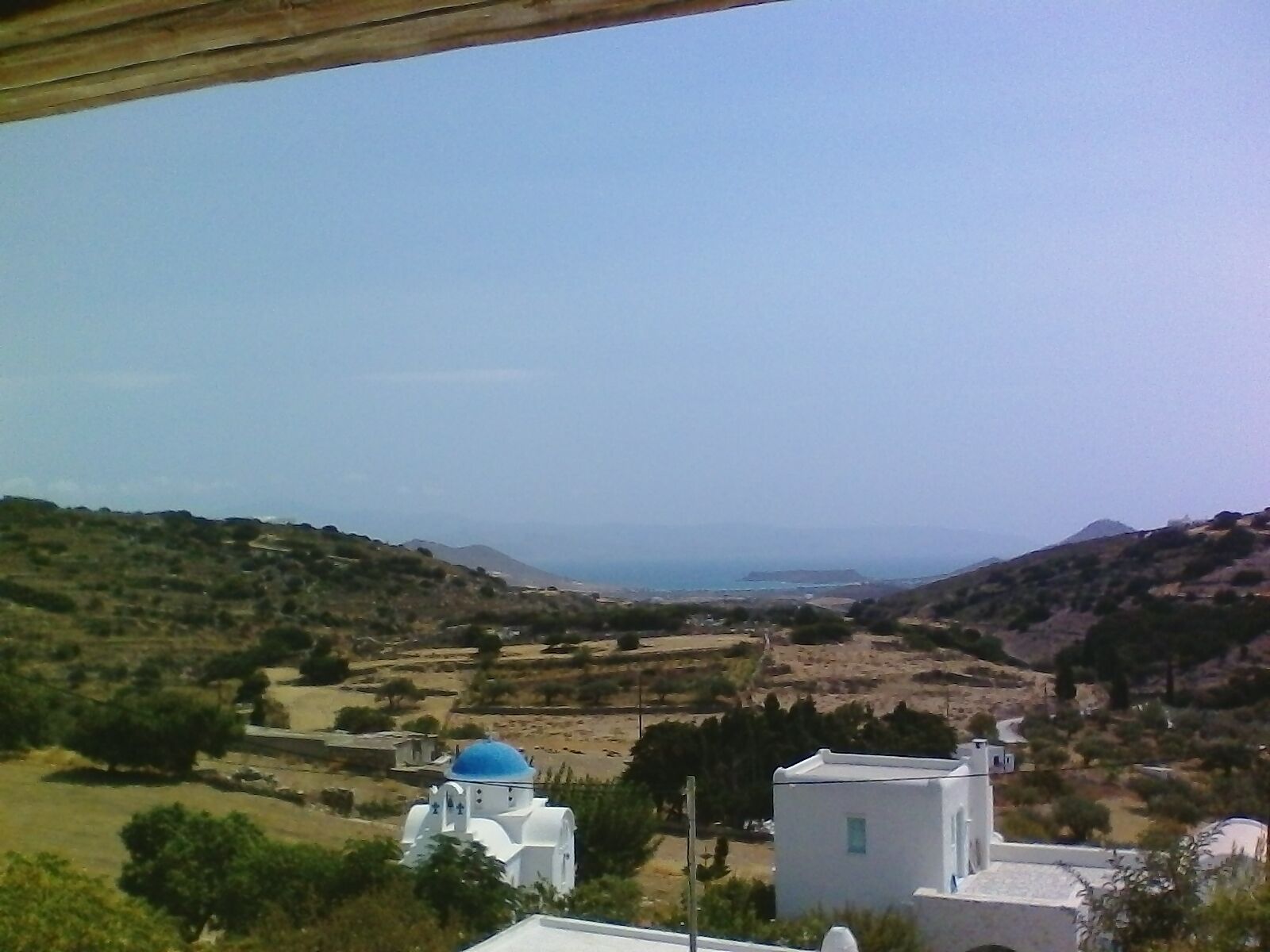 A coastal landscape with white buildings and a blue-domed structure, likely a church, surrounded by hills and a clear sky.