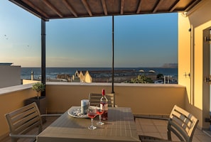 Ein Balkon mit Tisch für zwei Personen, einer Weinflasche und einer Kerze. Blick aufs Meer und ein entfernter Gebirgszug.