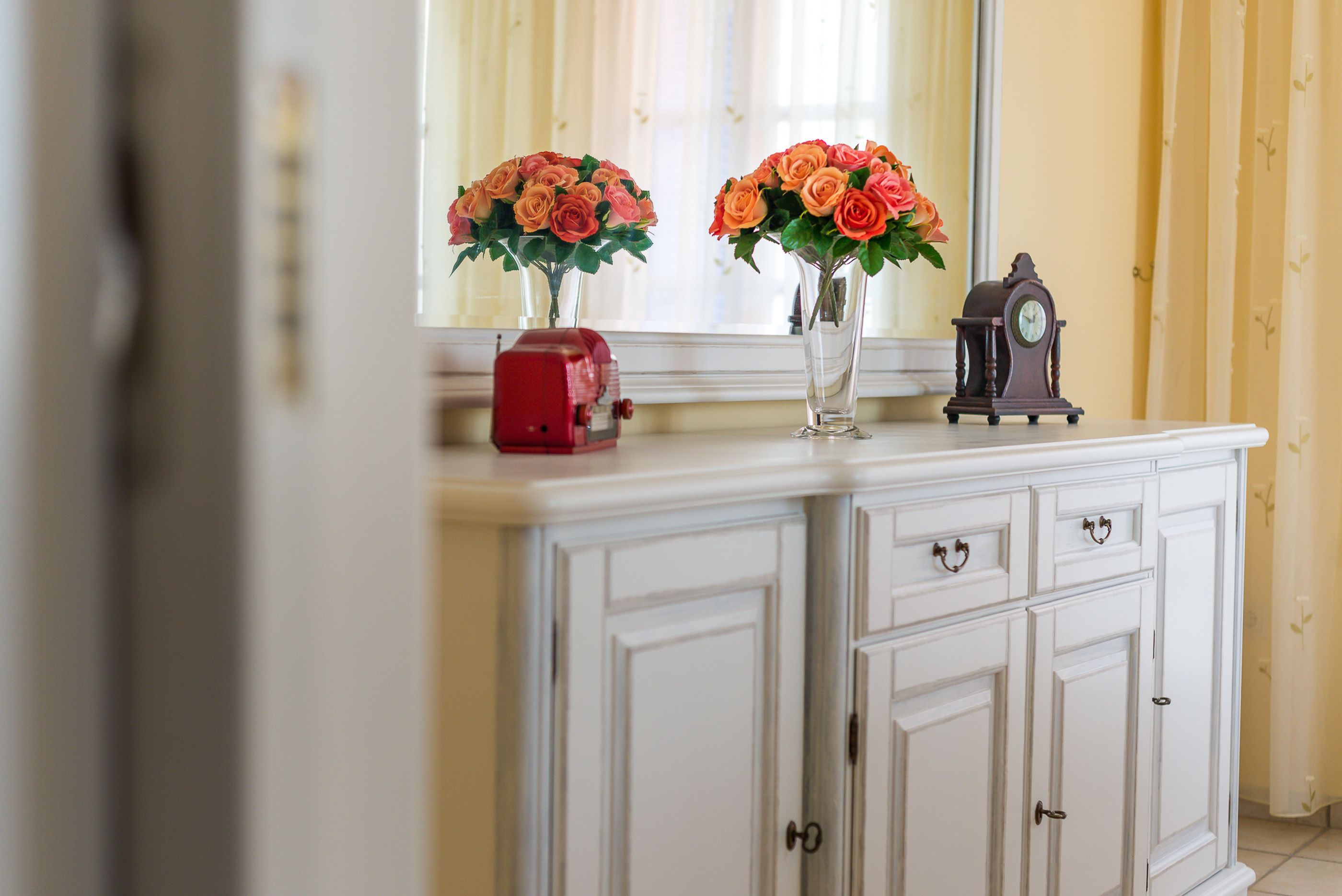 A white cabinet with two vases of roses and a small clock on top.
