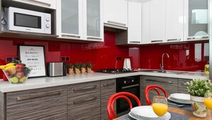 A modern kitchen with white cabinets, a red backsplash, and a dining area with a table set for two. - Otium Old Town Starowiślna (Kraków)