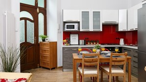 A compact kitchen with white and red cabinets, a microwave, and a dining area with wooden chairs and a table. - Otium Old Town Starowiślna (Kraków)
