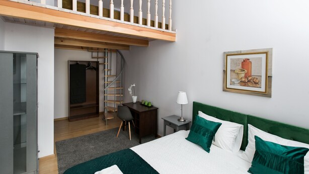 A bedroom with a bed, green pillows, a desk, a chair, a lamp, and a painting on the wall. - Otium Old Town Starowiślna (Kraków)