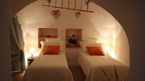 A cozy bedroom with two beds, a small table, and a shelf with decorative items. - Suite del Vico NEW OPENING! (Alberobello)