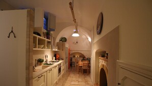 A narrow kitchen with white cabinets, a dining area with a checkered tablecloth, and a tiled floor. - Suite del Vico NEW OPENING! (Alberobello)