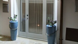 A building entrance with a covered entryway, two large potted plants, and a glass door with curtains. - Suite del Vico NEW OPENING! (Alberobello)