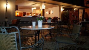 An outdoor seating area with round tables and chairs, potted plants, and wall-mounted lighting. - Historisches Wirtshaus an der Lahn (Lahnstein)
