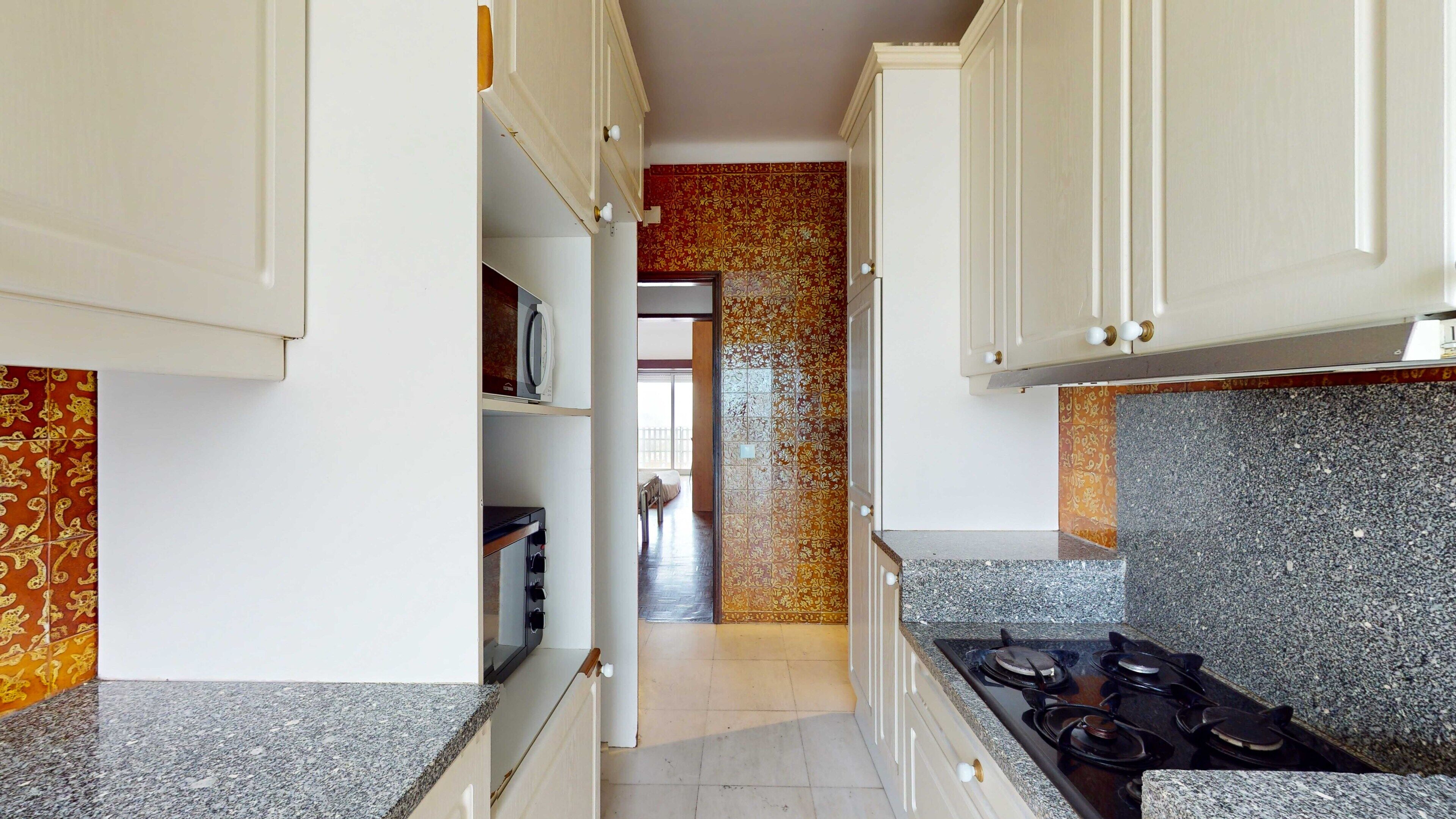 A narrow kitchen with white cabinets, a granite countertop, and a stove.
