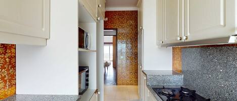 A narrow kitchen with white cabinets, a granite countertop, and a stove.