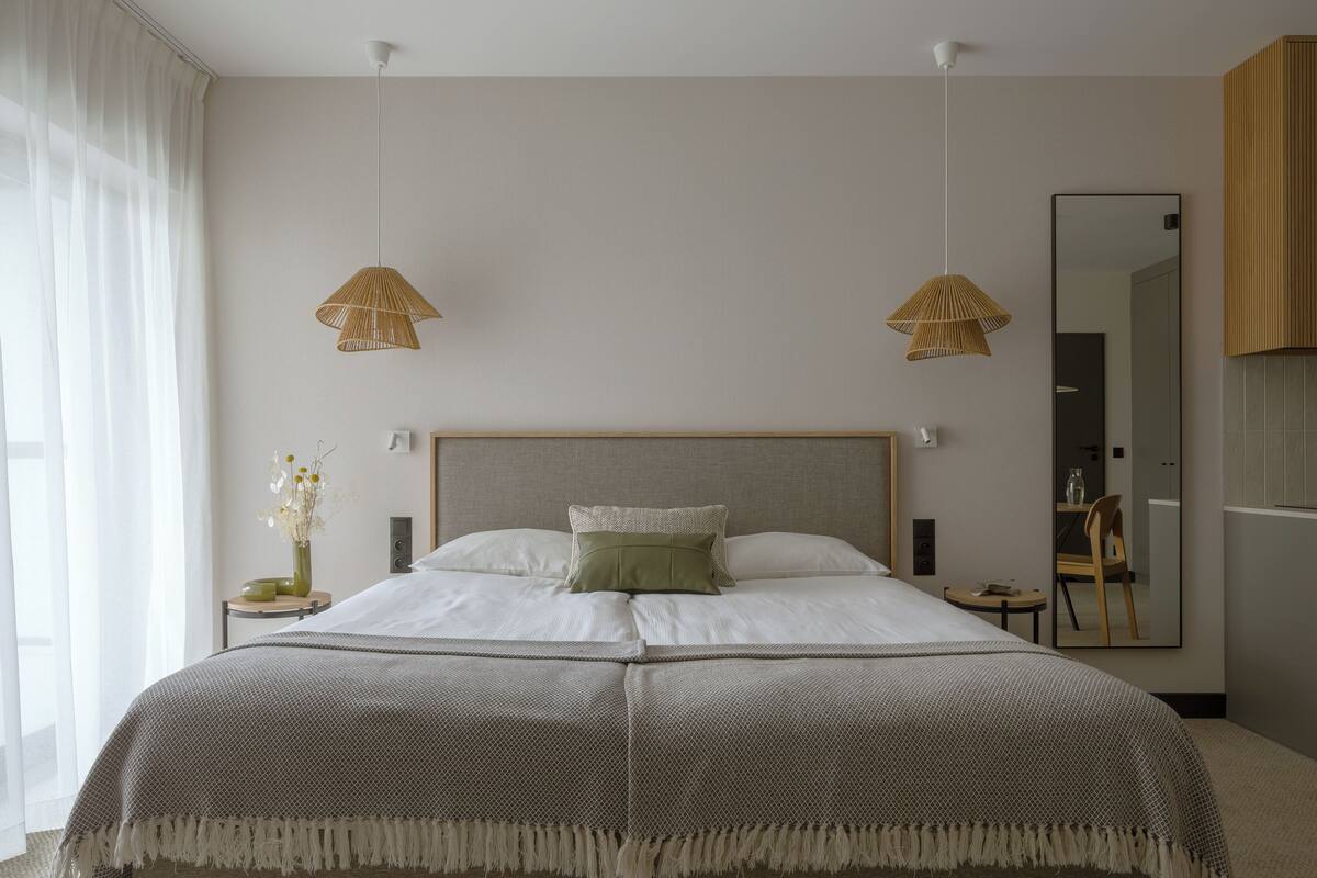 A modern hotel room with a large bed, two bedside lamps, a mirror, and a small table with a vase of flowers.