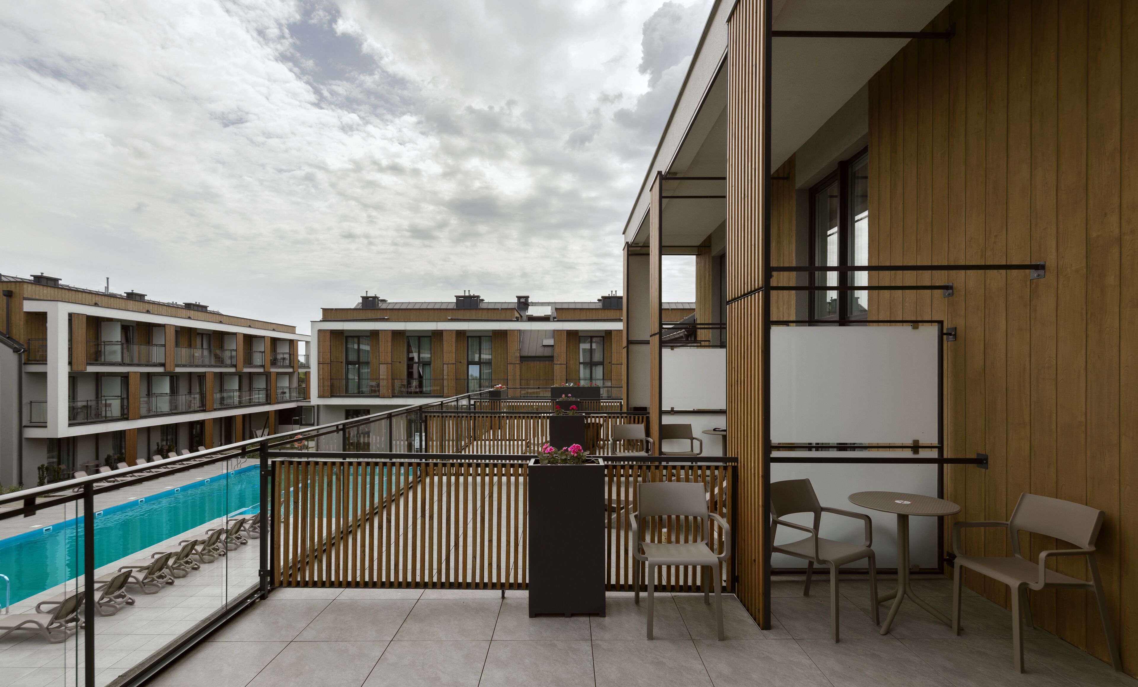 A modern outdoor balcony with a pool, wooden railings, and seating.