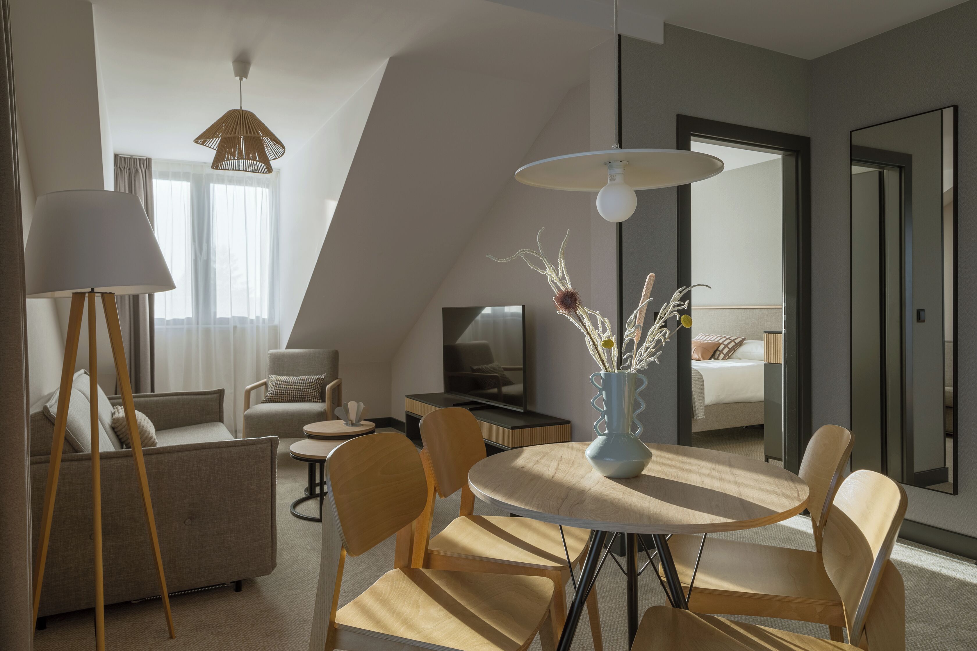 A modern hotel room with a dining area, a sofa, a TV, and a large mirror.