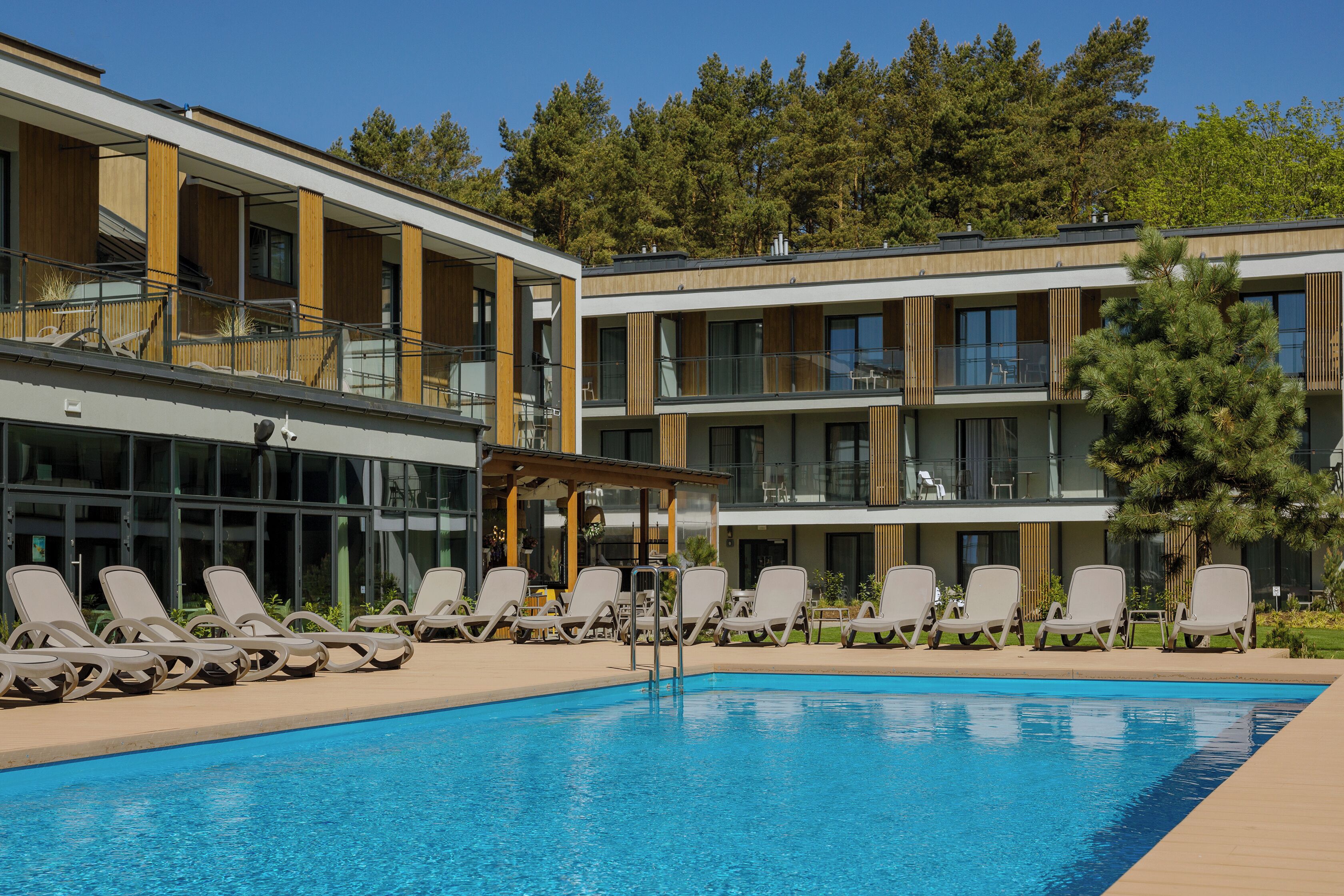 A modern hotel with a pool area, multiple balconies, and a view of the surrounding forest.