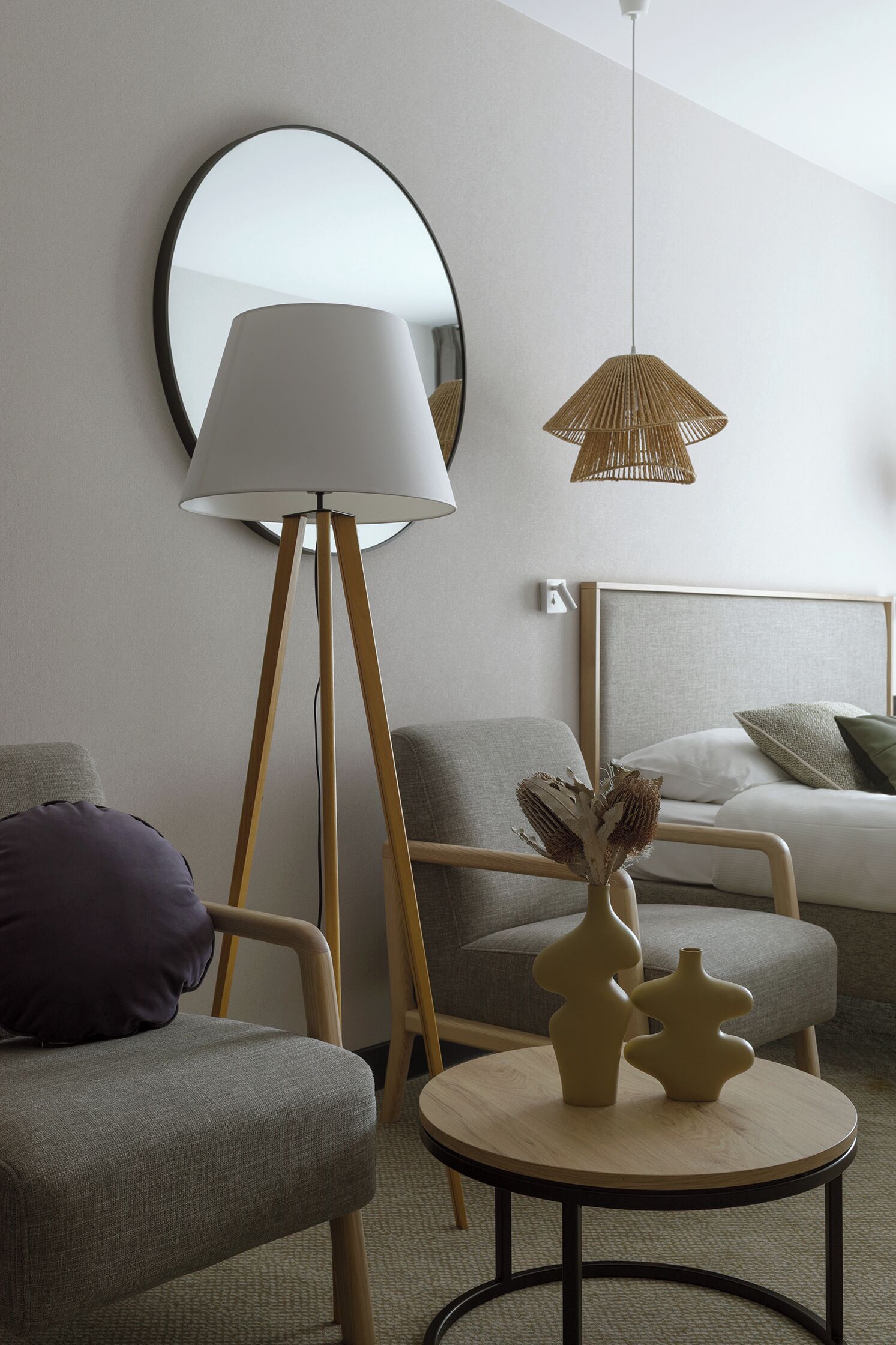 A modern hotel room with a round table, a floor lamp, a round mirror, and a bed with a headboard.