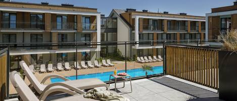 A rooftop pool area with sun loungers, a small table with a drink, and a view of the pool.