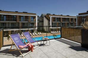 A rooftop terrace with two lounge chairs, a small table with a drink, and a pool area. - Saltic Resort & Spa Grzybowo (Grzybowo)