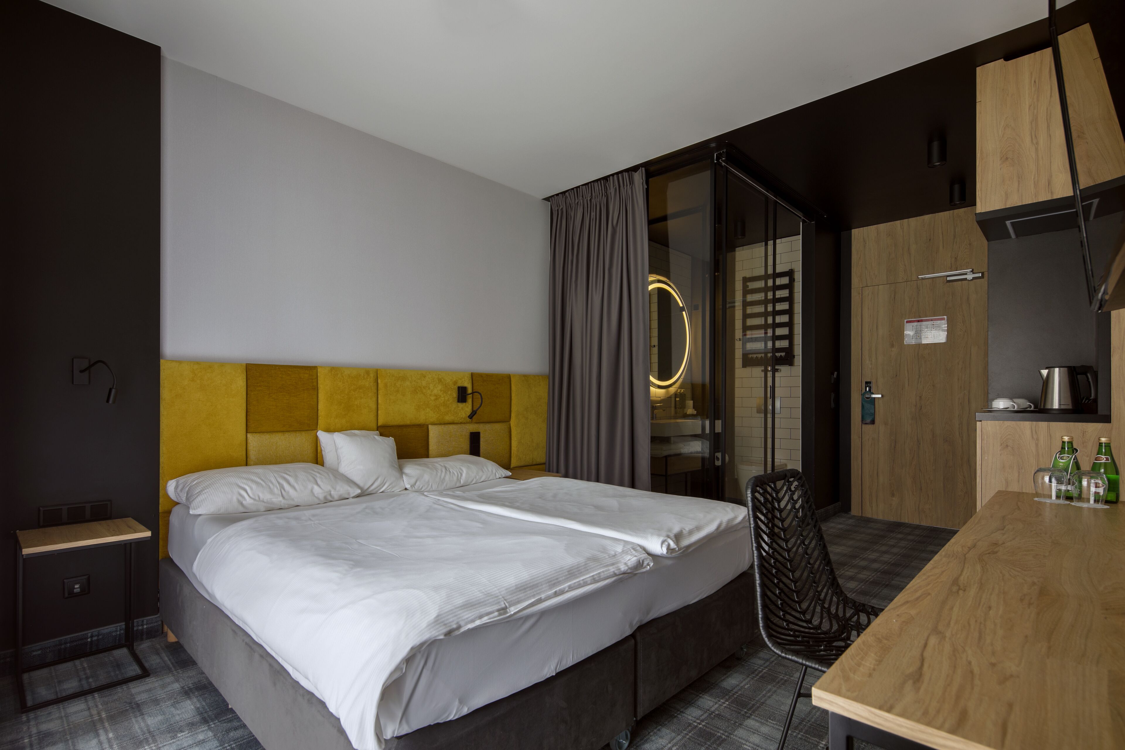 Una habitación de hotel con una cama grande, un escritorio de madera, una silla y una mesita con botellas.