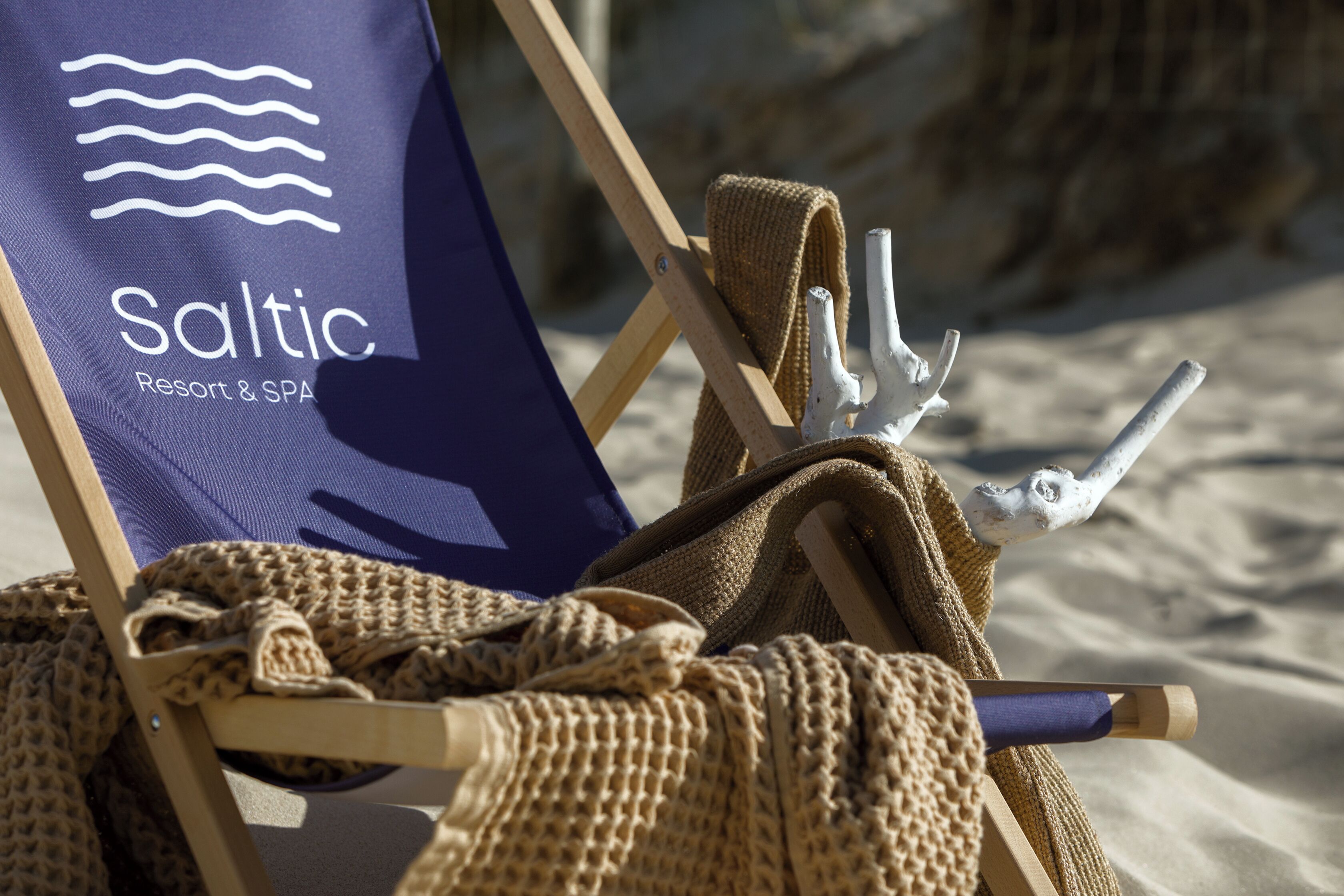 Una silla de playa con una toalla con la marca 'Saltic Resort & SPA' y un descortezador de hielo metálico.