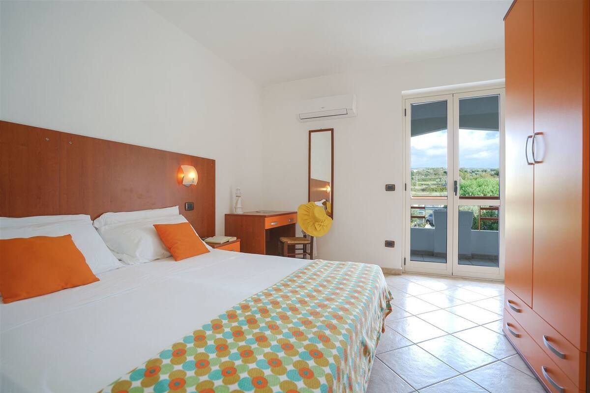 Ein Hotelzimmer mit Bett, Schreibtisch, Stuhl, Spiegel und einer Glastür zum Balkon.