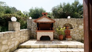 Una chimenea de piedra al aire libre con una chimenea de ladrillo, rodeada de muros de piedra y plantas en macetas.