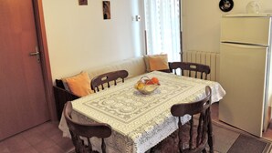 Un coin repas avec une table dressée pour deux personnes, un canapé, un réfrigérateur et des éléments de décoration murale, notamment des horloges et des assiettes.
