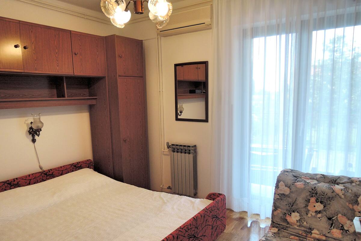 A bedroom with a large bed, wooden wardrobe, radiator, and a floral-patterned sofa.