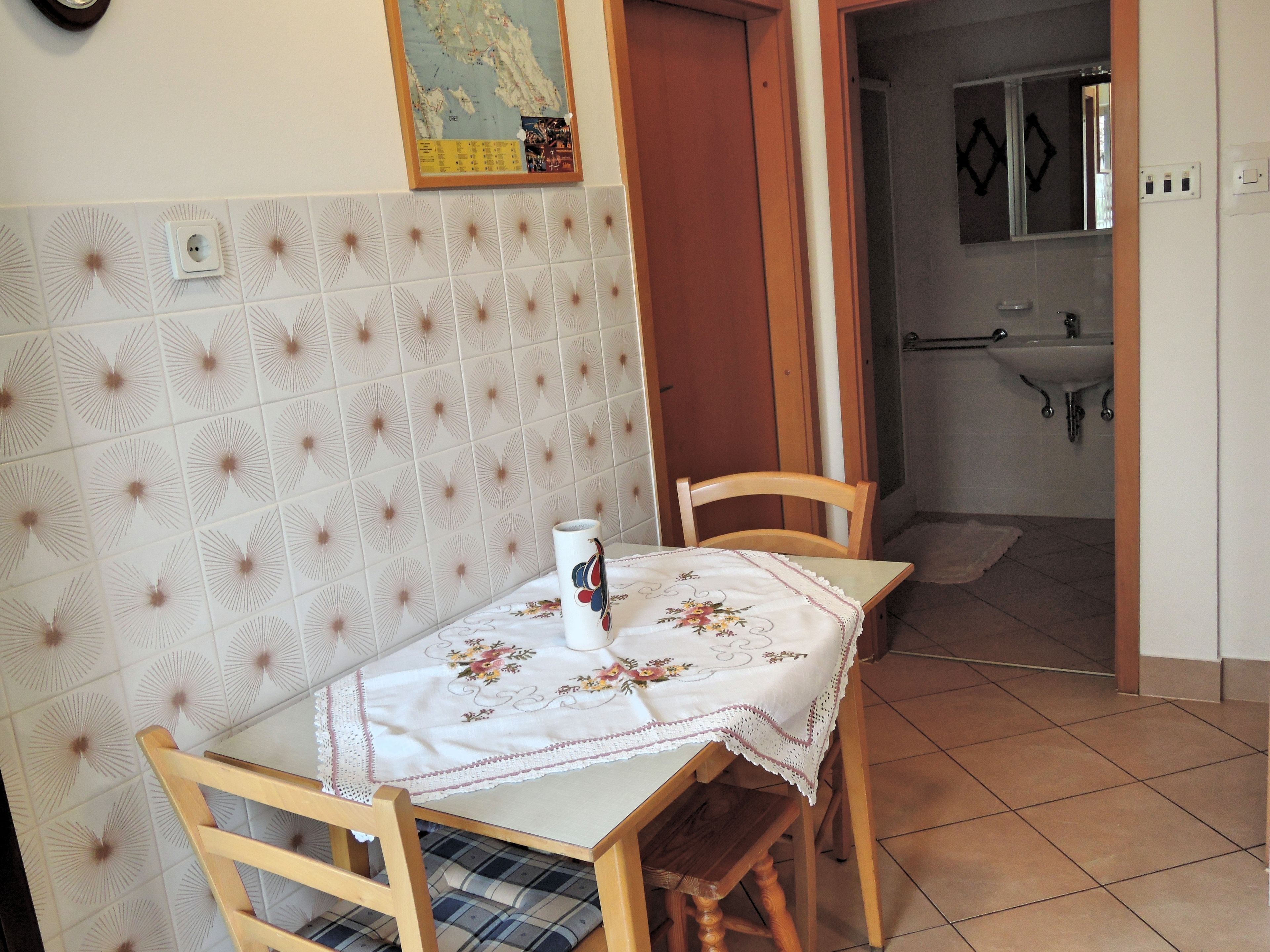 A small dining area with a table covered by a floral tablecloth, two wooden chairs, and a wall-mounted map.