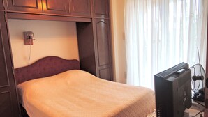 Une chambre à coucher avec un lit, une télévision et une fenêtre avec des rideaux.