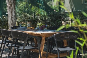 A round wooden table with a glass top, surrounded by four wicker chairs. A glass pitcher and a bowl of fruit are on the table. - Mid-Century Modern Villa Vintage Charm (Platanias)