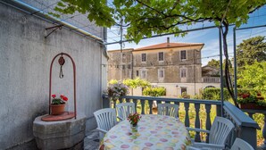 A balcony with a table and chairs, a hanging plant, and a building in the background. - Apartment Anica (Malinska-Dubasnica)
