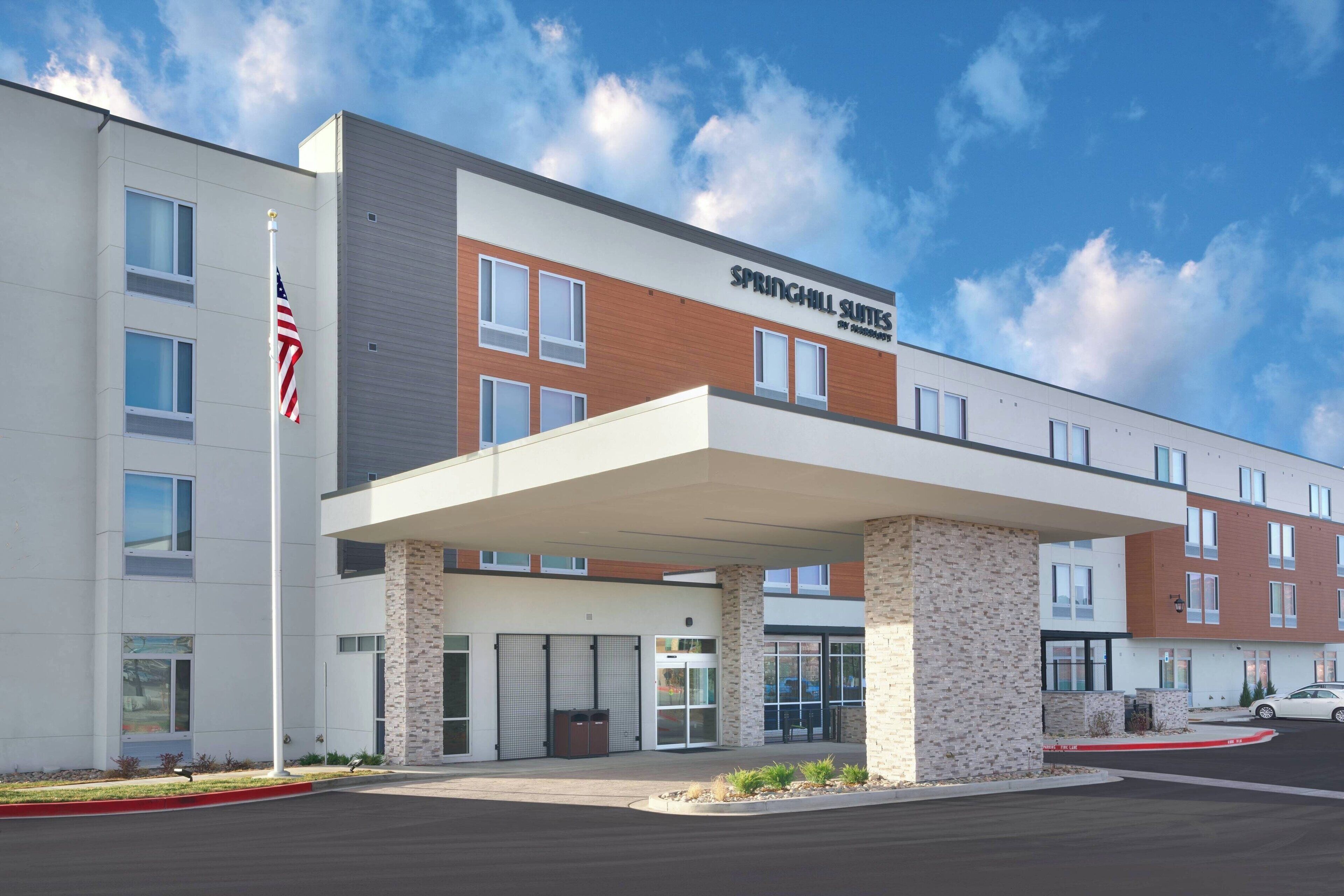 Un hotel moderno con entrada cubierta, una bandera y un letrero que dice "SPRINGHILL SUITES".
