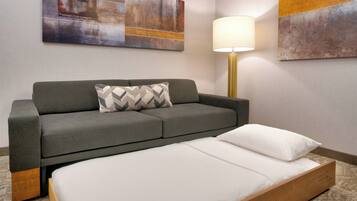 Quarto de hotel moderno com sofá cinzento, estrutura de cama de madeira e uma grande pintura abstrata na parede.