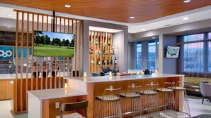 Un área de bar moderna con mostrador de madera, taburetes, una televisión y una vitrina de licores.