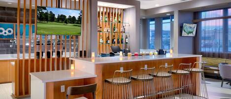 A modern bar area with a wooden counter, bar stools, a television, and a liquor display.