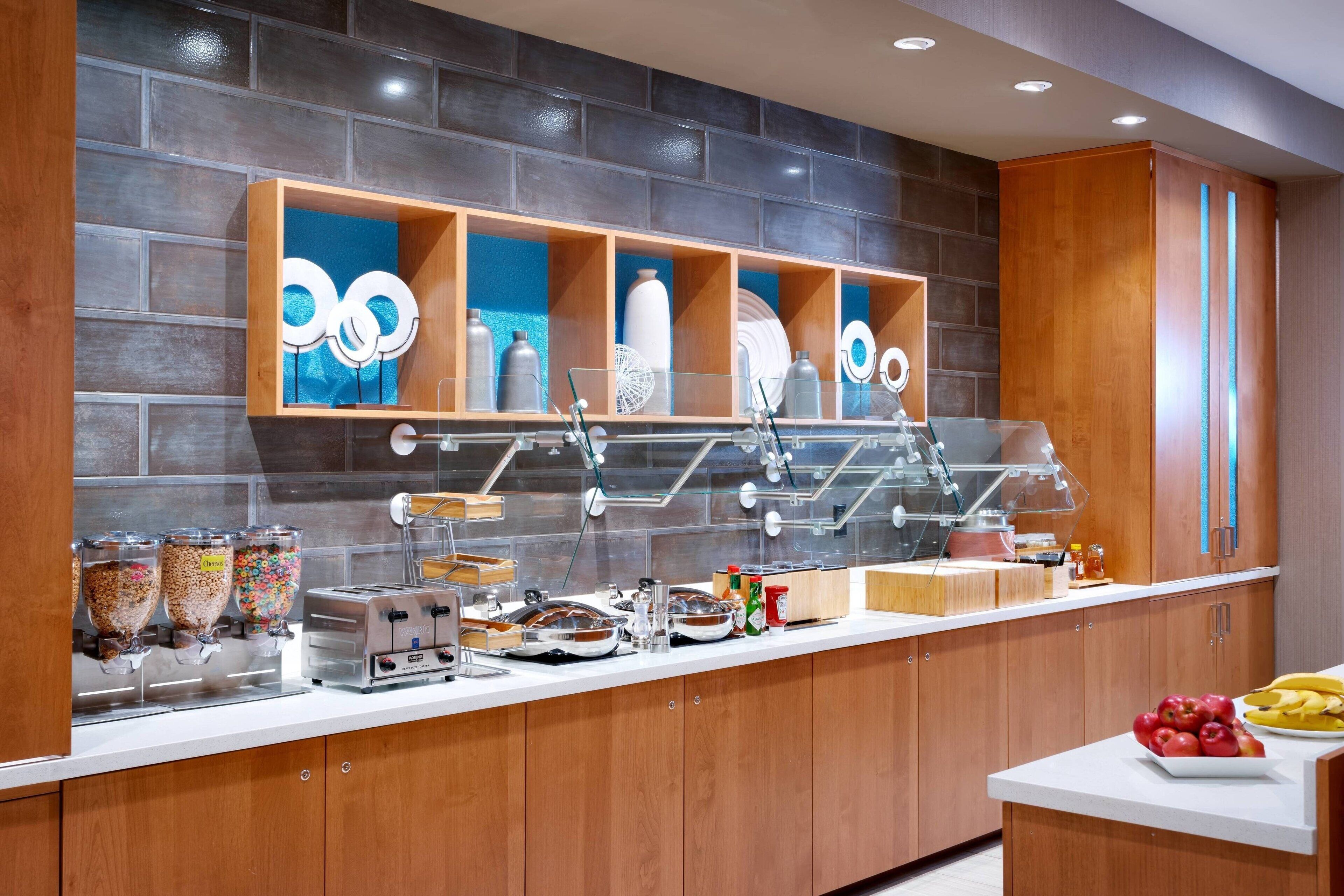 A modern kitchen with a brick wall, wooden cabinets, and a countertop with various appliances and food items.